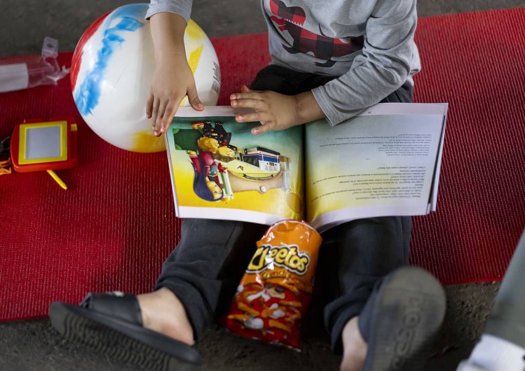 A young immigrant boy reads with his book "Homecoming" By Margarita Quiñones-Peña at the Pilsen shelter on July 9, 2023. 
