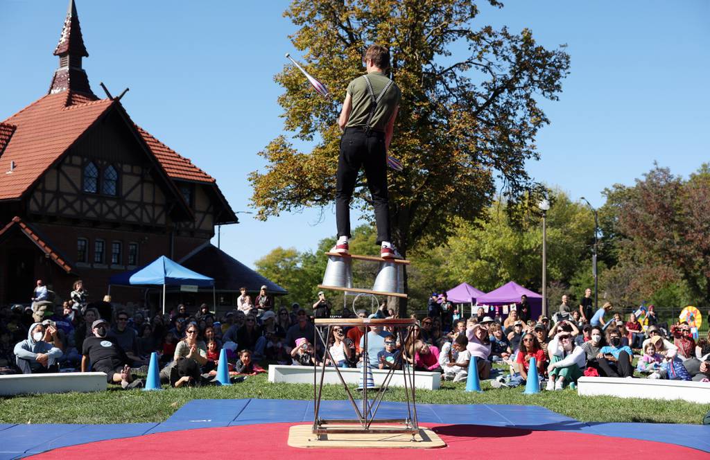 Midnight Circus member Max Jenkins balances on a stacked plank, a second plank, and a roller as he juggles during his performance at Humboldt Park in Chicago on October 1, 2022.