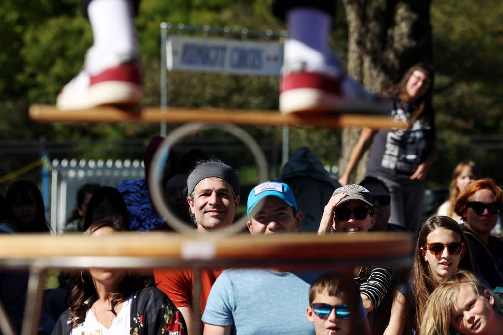 People watch Midnight Circus member Max Jenkins balance on a board above the roller during his performance at Chicago's Humboldt Park on October 1, 2022.