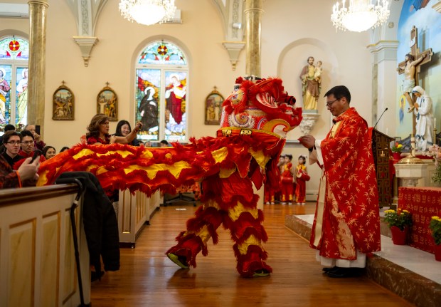 Father Frances Li at St. Peter's Church in Chinatown on February 11, 2024.  Therese presents the gift of a red envelope during the lion dance during Lunar New Year celebrations at the Chinese Catholic Church.  (Brian Cassella/Chicago Tribune)