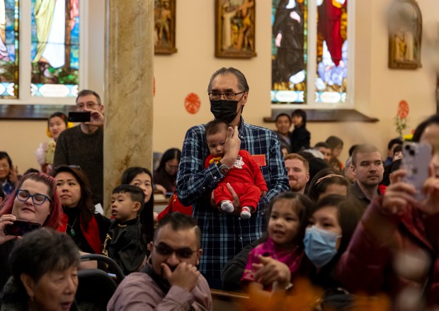 On February 11, 2024, at St. Petersburg in Chinatown.  A man covers a baby's ears as fireworks explode outside to begin Lunar New Year celebrations at Therese Chinese Catholic Church.  (Brian Cassella/Chicago Tribune)