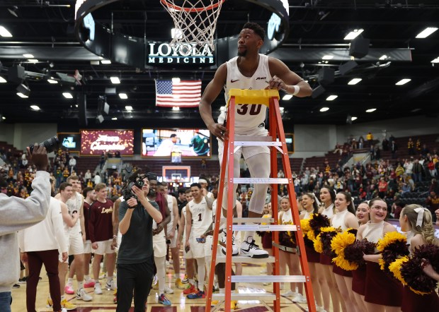 Loyola forward Patrick Mwamba climbs a ladder to cut off a piece of the net after beating La Salle 64-54 for a share of the Atlantic 10 title on March 9, 2024 at Gentile Arena.  (John J. Kim/Chicago Tribune)